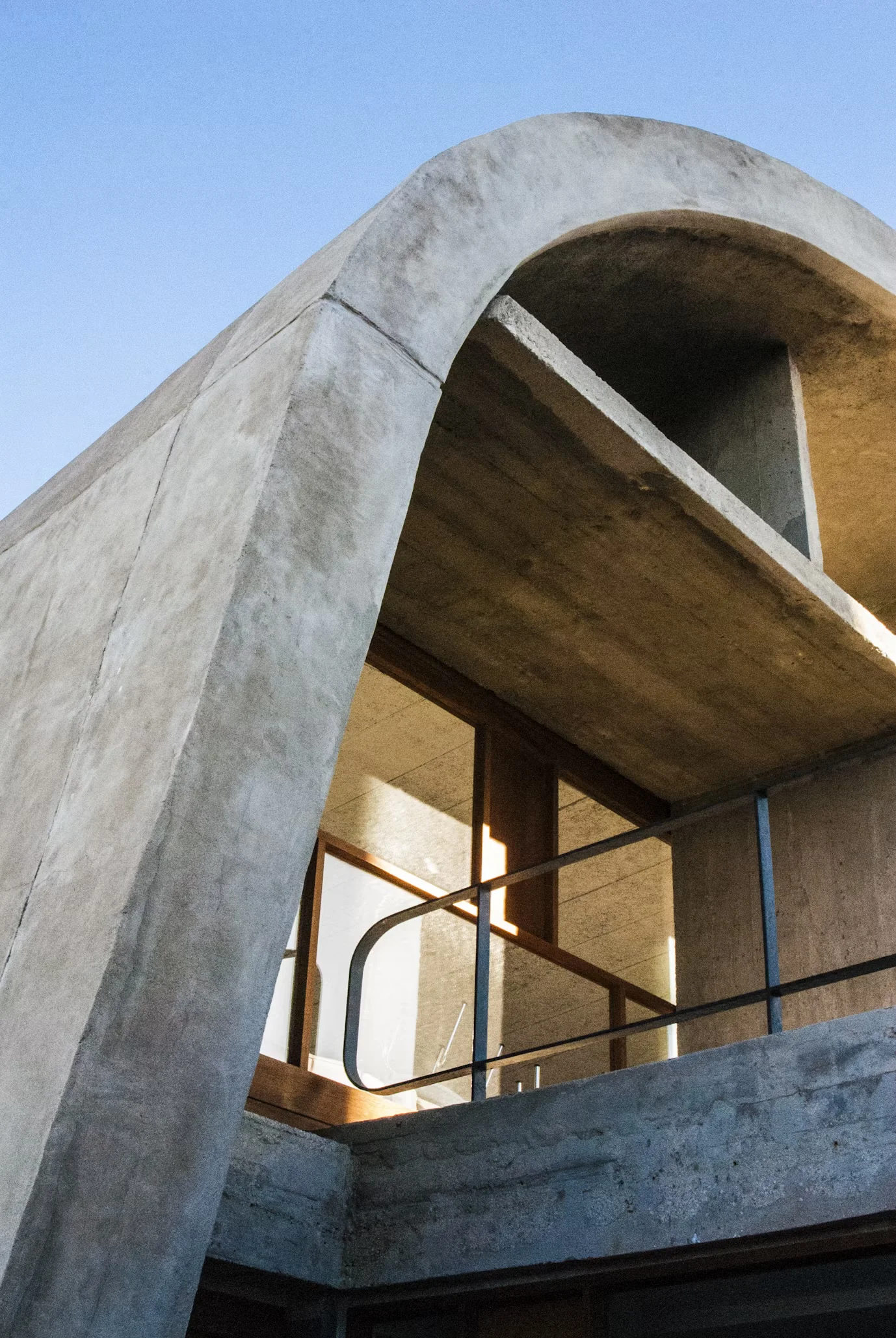 Curved exposed-concrete facade with a balcony and deep concrete floor edges