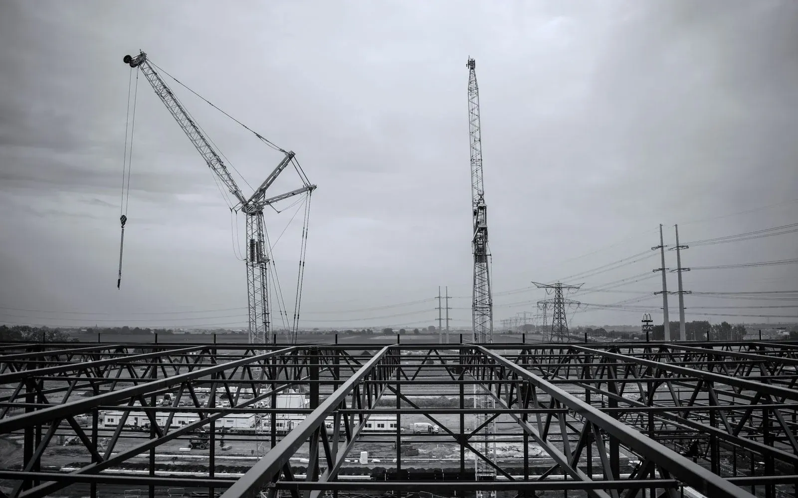 Illustrative monochrome construction photograph of an erected steel roof frame with cranes behind it