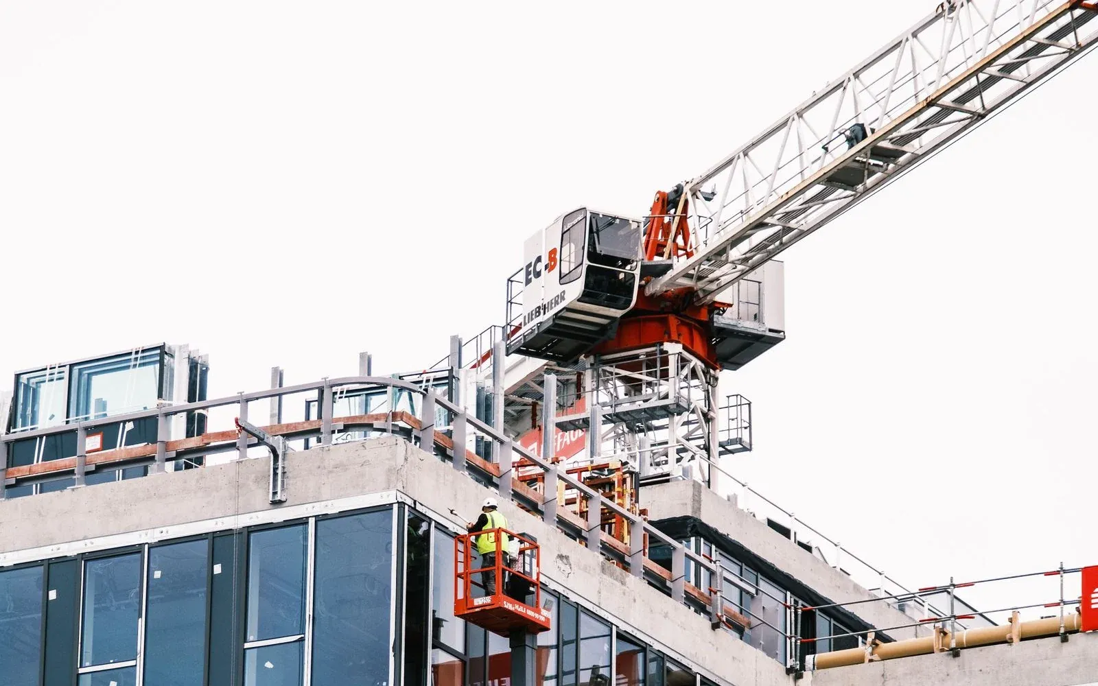 Illustrative construction photograph of a tower crane and a worker installing a modern glass facade