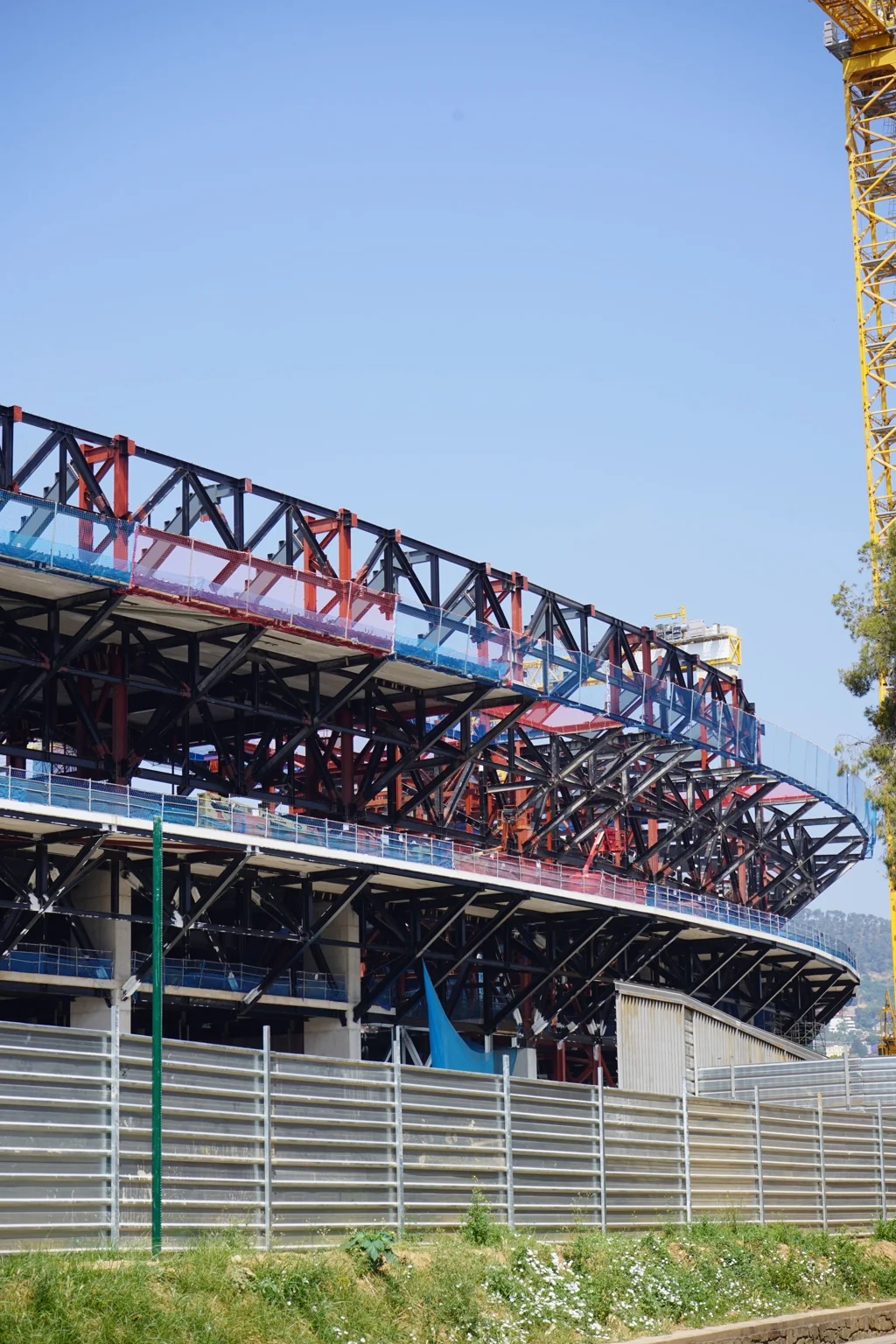 Multi-level steel structure under construction with exposed trusses, temporary barriers and a tower crane